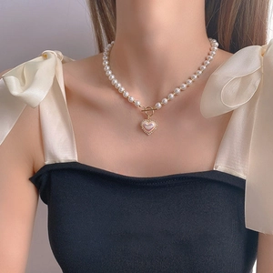 Detail of pearl heart necklace with gold toggle clasp and iridescent center on model