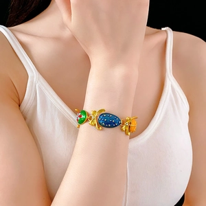 Dettaglio macro del bracciale vintage placcato oro con fiocco e ciondoli in smalto