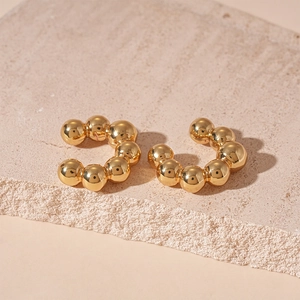 Detail of C-shaped gold metal ear cuff with smooth geometric beads on a stone surface