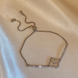 Détail du bracelet trèfle argenté avec incrustation blanche sur satin champagne