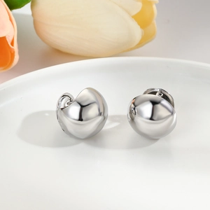 Macro shot of silver geometric hollow ball hoop earrings on a white ceramic plate