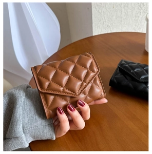 Close-up of a brown quilted leather clutch wallet held by a woman in a cafe setting