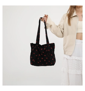 Detail of black corduroy shoulder bag featuring an all-over red strawberry print pattern