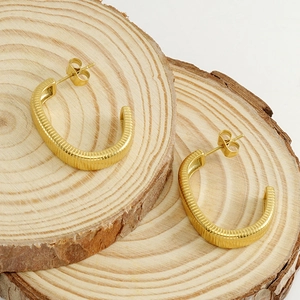 Makrodetail von 18K vergoldeten C-förmigen Creolen mit geripptem Texturdesign und Stil