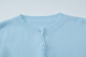Detail of light blue knit cardigan featuring ribbed crew neck and matching resin buttons