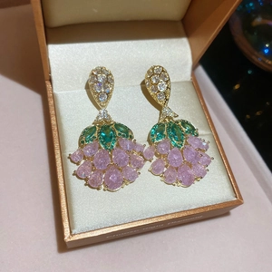 Macro detail of gold flower earrings with green leaves and pink crystal drops in a box