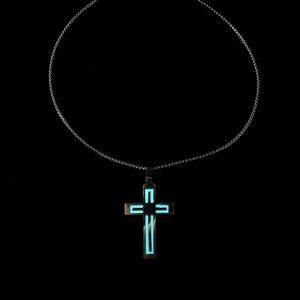 Luminous cross pendant glowing in the dark with blue-green light on a dark chain