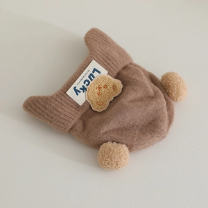 Detail of dark brown baby beanie showing soft plush poms and lucky bear patch embroidery