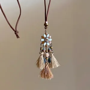 Détail du collier bohème avec marguerite en émail, pompons et cordon en daim brun