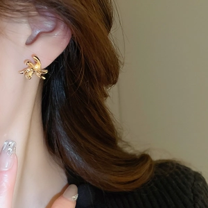 Detailed view of model wearing gold abstract twisted flower stud earrings in a minimalist style