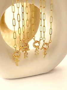 Close-up of golden paperclip chain necklaces with zircon-studded alphabet pendants