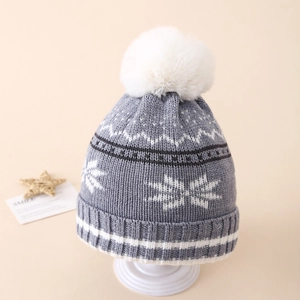 Detailed close-up of a grey winter knit hat with white snowflakes and a fluffy pom-pom