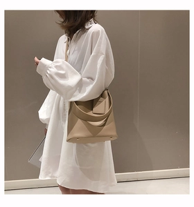 Side view of a minimalist beige bucket bag with metal feet on a white shirt model