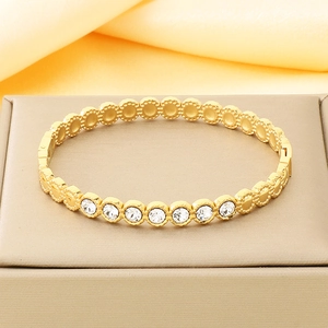 Gros plan sur un bracelet jonc en acier titane doré avec zircons et fermoir sur satin