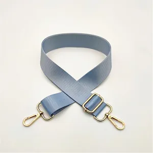 Detail of light blue nylon bag strap with polished gold-tone metal buckles and lobster clasps