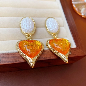 Dettaglio di orecchini vintage con ovale bianco e cuore in resina arancione lucida