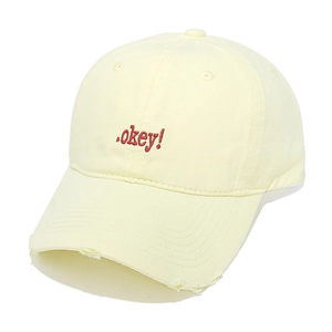 Detail of red '.okey!' embroidery on a light yellow distressed cotton baseball cap