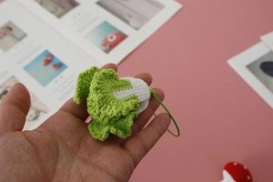 Close-up of a handmade crochet Napa cabbage pendant held in hand for size display