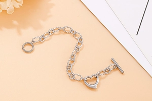 Close-up of heart charm bracelet with textured chain links and silver OT toggle clasp