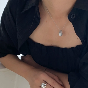 Detail of model wearing a silver heart pendant necklace and wide minimalist ring