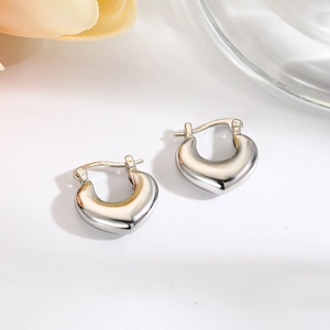 Macro shot of silver heart-shaped hoop earrings on a minimalist white table with flowers