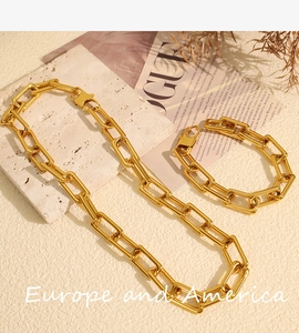 Chunky gold-plated chain necklace and bracelet set displayed on a stone pedestal