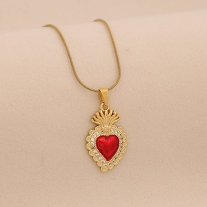 Close-up of a gold heart pendant with red zircon and crown detail on a snake chain