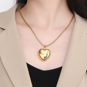 Detail of a large hollow gold heart pendant and snake chain on a female model