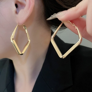 Close-up of a model wearing minimalist gold rhombic geometric hoop earrings