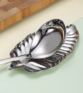 Detail view of a polished leaf-shaped stainless steel spoon rest and matching silver spoon