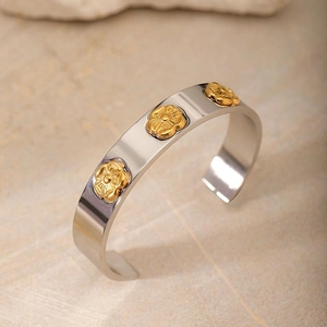 Detail of silver stainless steel open cuff bracelet with three 3D golden flower accents