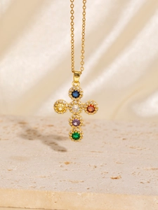 Close-up of golden cross necklace with multi-colored stones against silk background