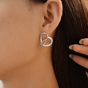 Detail of silver heart-shaped earrings with hammered texture on female model's ear