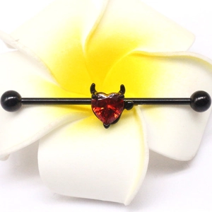 Macro view of black industrial barbell with red heart gemstone and devil wings on white flower