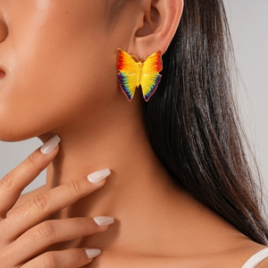 Close-up of model wearing vibrant gradient butterfly stud earrings in colorful enamel
