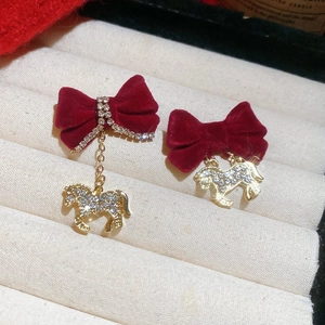Détail de boucles d'oreilles nœud velours rouge avec pendentif cheval doré et strass