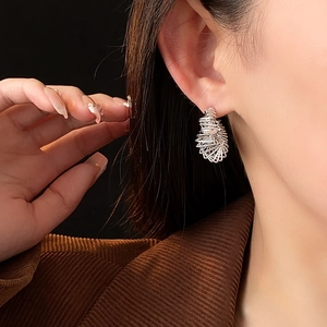 Close-up of twisted silver C-shape earring with intricate hollow spiral design on model