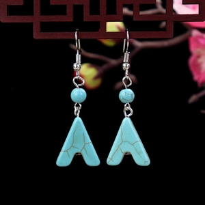 Detail of vintage turquoise drop earrings with floral accents on a wooden lattice stand