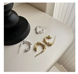 Macro detail of silver and gold twisted knot hoop earrings on a neutral surface