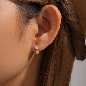Close-up of golden hoop earring featuring three heart-shaped crystals on ear