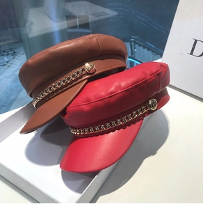 Close-up of red and brown faux leather baker boy hats with golden chain details