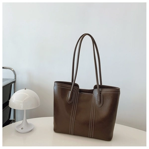 Detailed view of dark brown leather tote bag with contrasting white stitching on white table