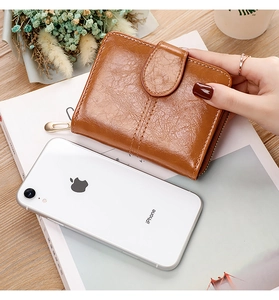 Brown leather short wallet size comparison with iPhone on magazine and wooden desk