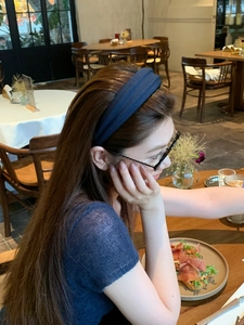 Detail of a navy blue fabric headband worn by a model in a cozy restaurant setting
