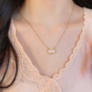 Gros plan d'un collier plaqué or 18 carats avec pendentif rectangulaire blanc sur modèle
