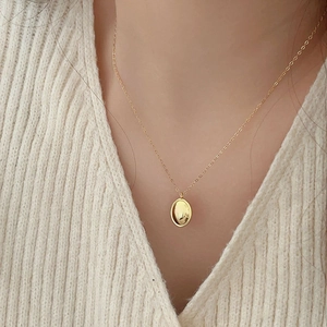 Close-up of minimalist gold oval pendant necklace on a beige knit cardigan sweater