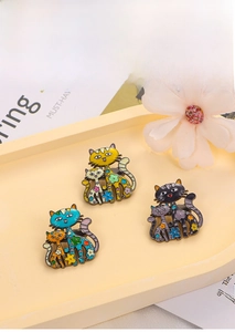 Trois broches chat en émail aux motifs floraux en jaune, bleu et violet couleurs