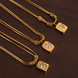 Triple golden layered snake chain necklaces with heart-shaped gemstone pendant on wood