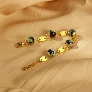Detailed macro view of a gold titanium steel bracelet with green resin beads on silk