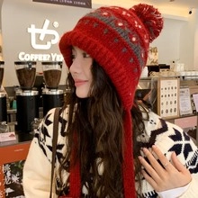Asiatisches Model trägt eine gemütliche rot-graue Strickmütze mit Ohrenklappen